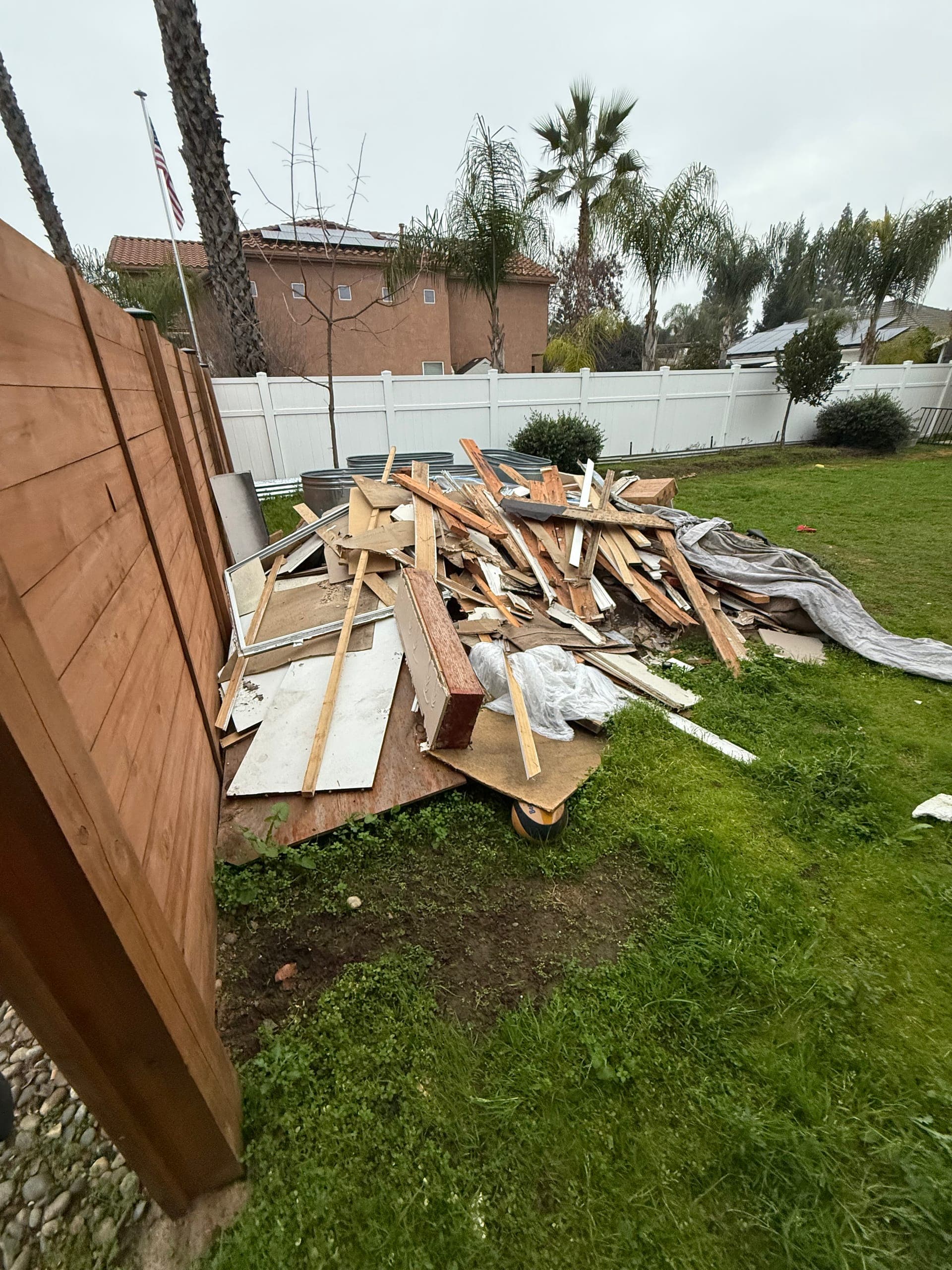 Backyard lawn buried under a pile of old lumber and fencing before haul-away