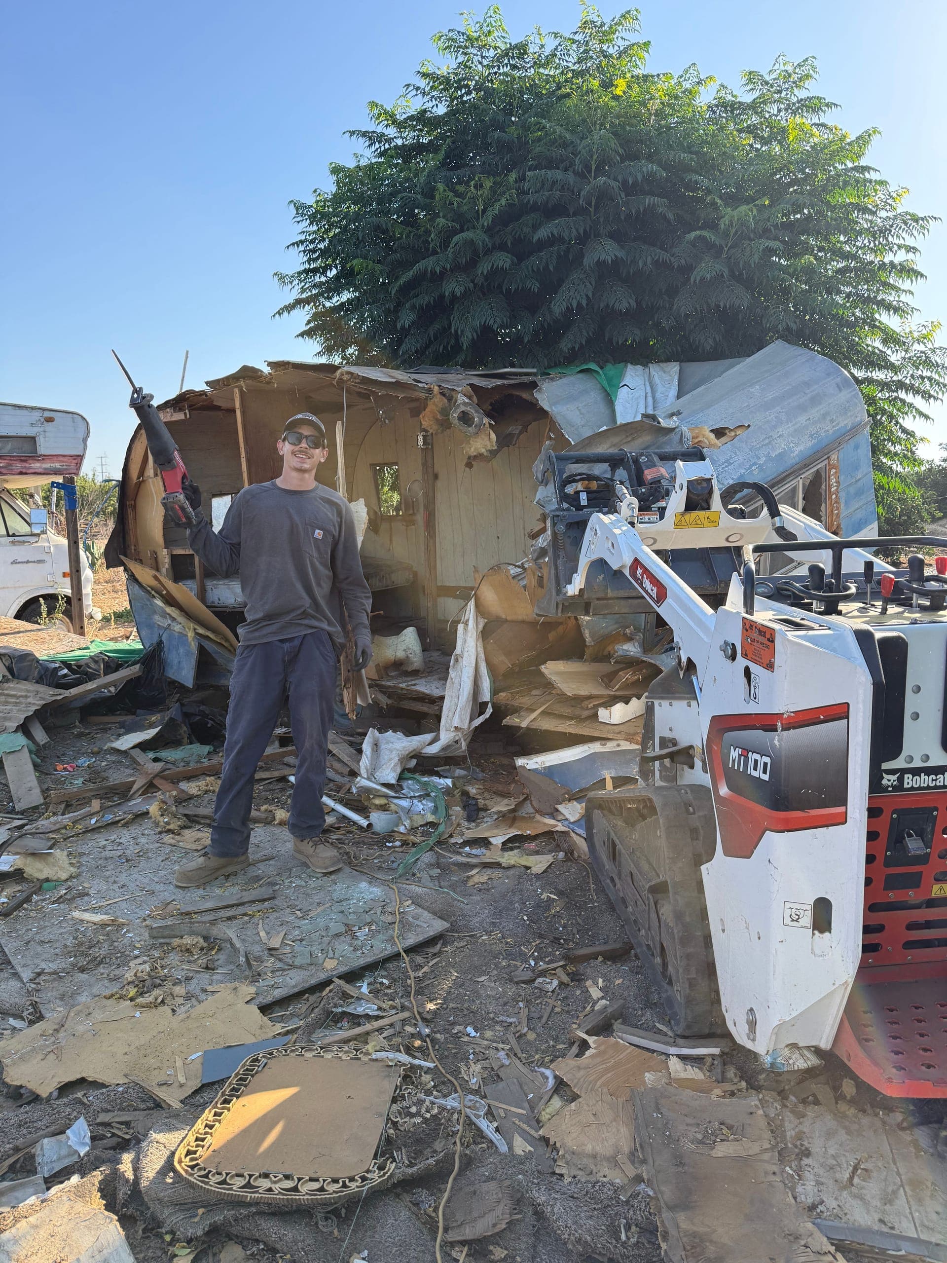 Papi's crew member beside a Bobcat MT100 mini track loader at a backyard structure teardown near Sanger