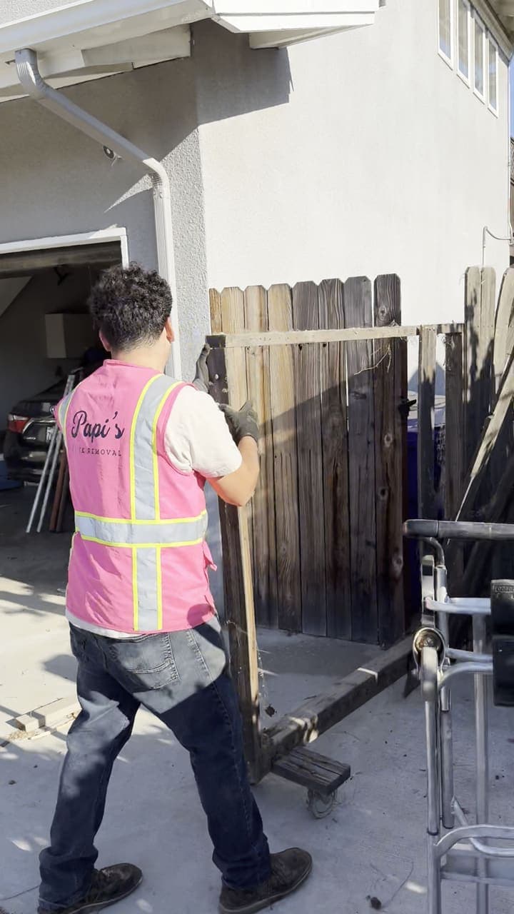 Papi’s crew member in a pink vest moving old fence panels out of a garage in Fresno