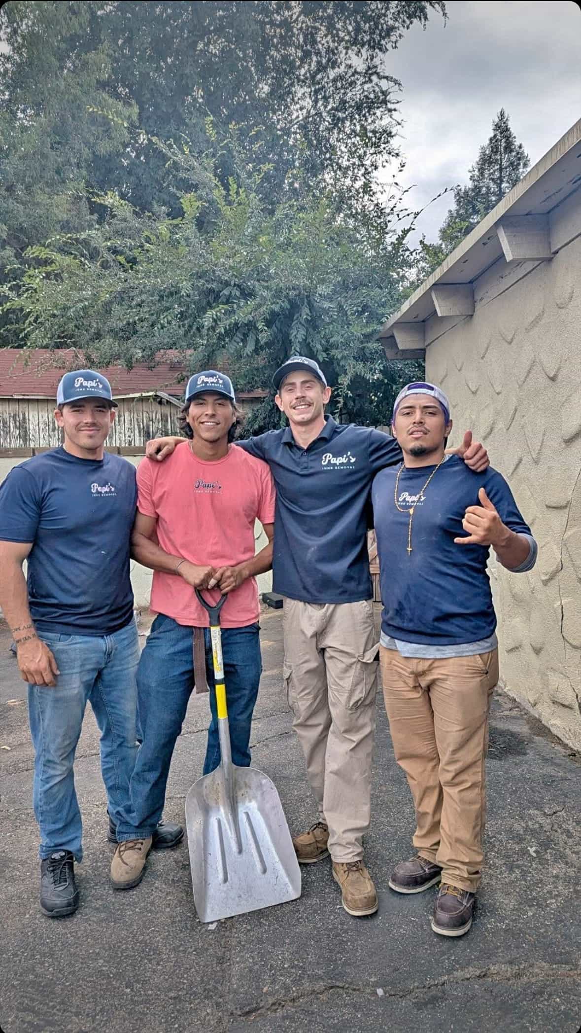 Four Papi's Junk Removal crew members in navy and pink shirts holding a shovel