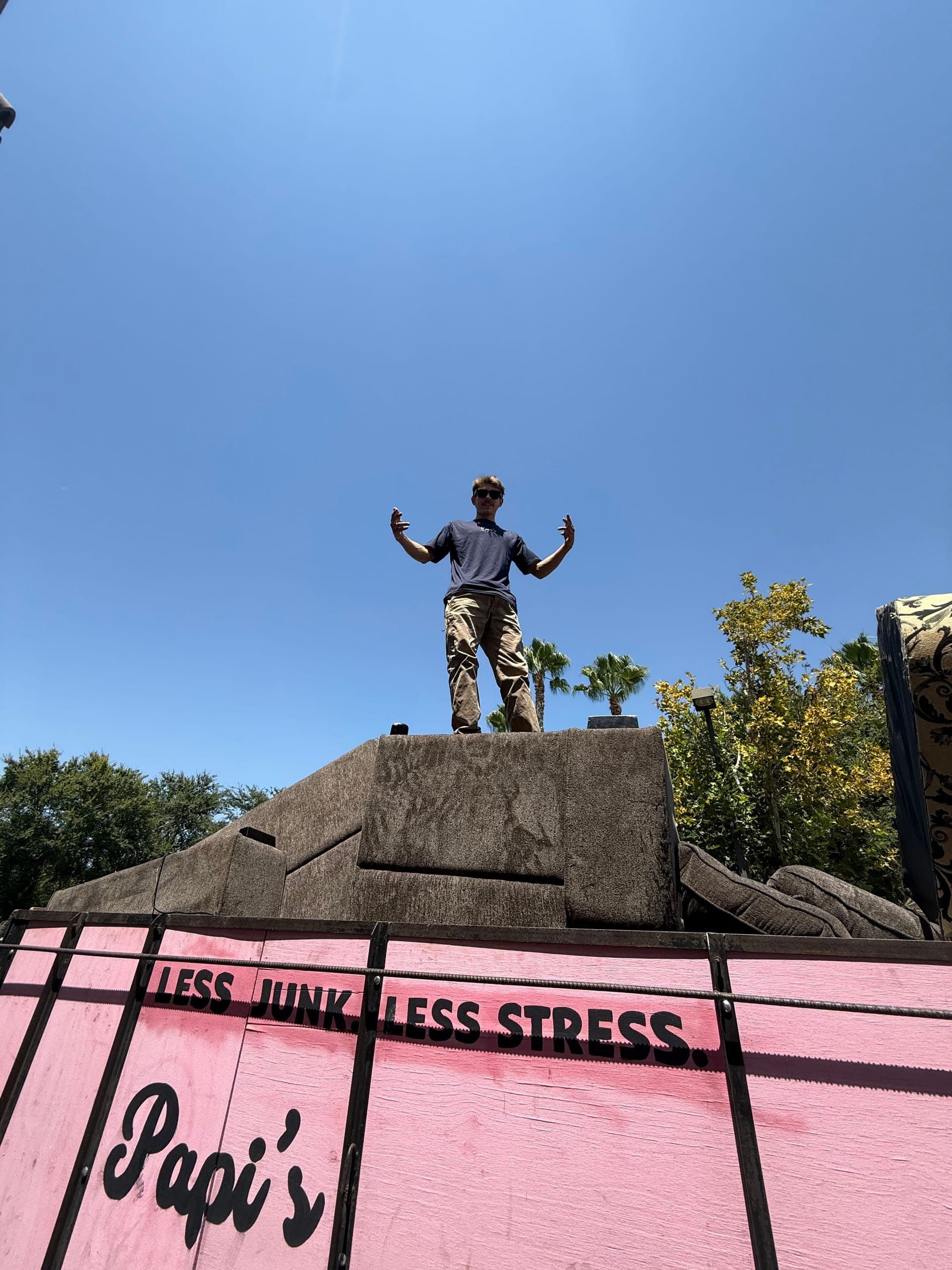 Un muchacho de Papi's parado encima de un tráiler rosa lleno que dice 'Less Junk. Less Stress.' en Clovis