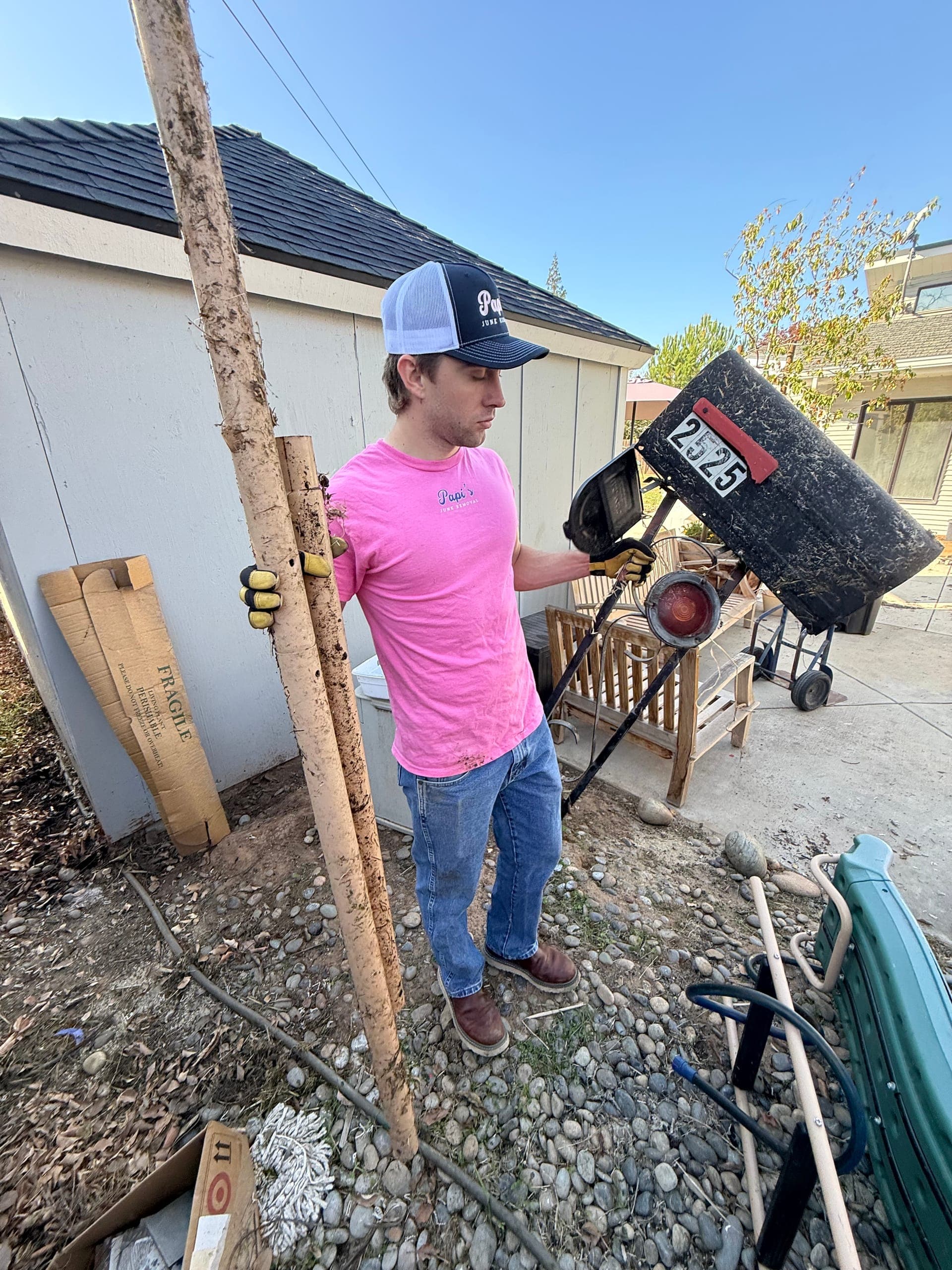Papi's crew member in a pink shirt hauling an old tire and fence post out of a backyard
