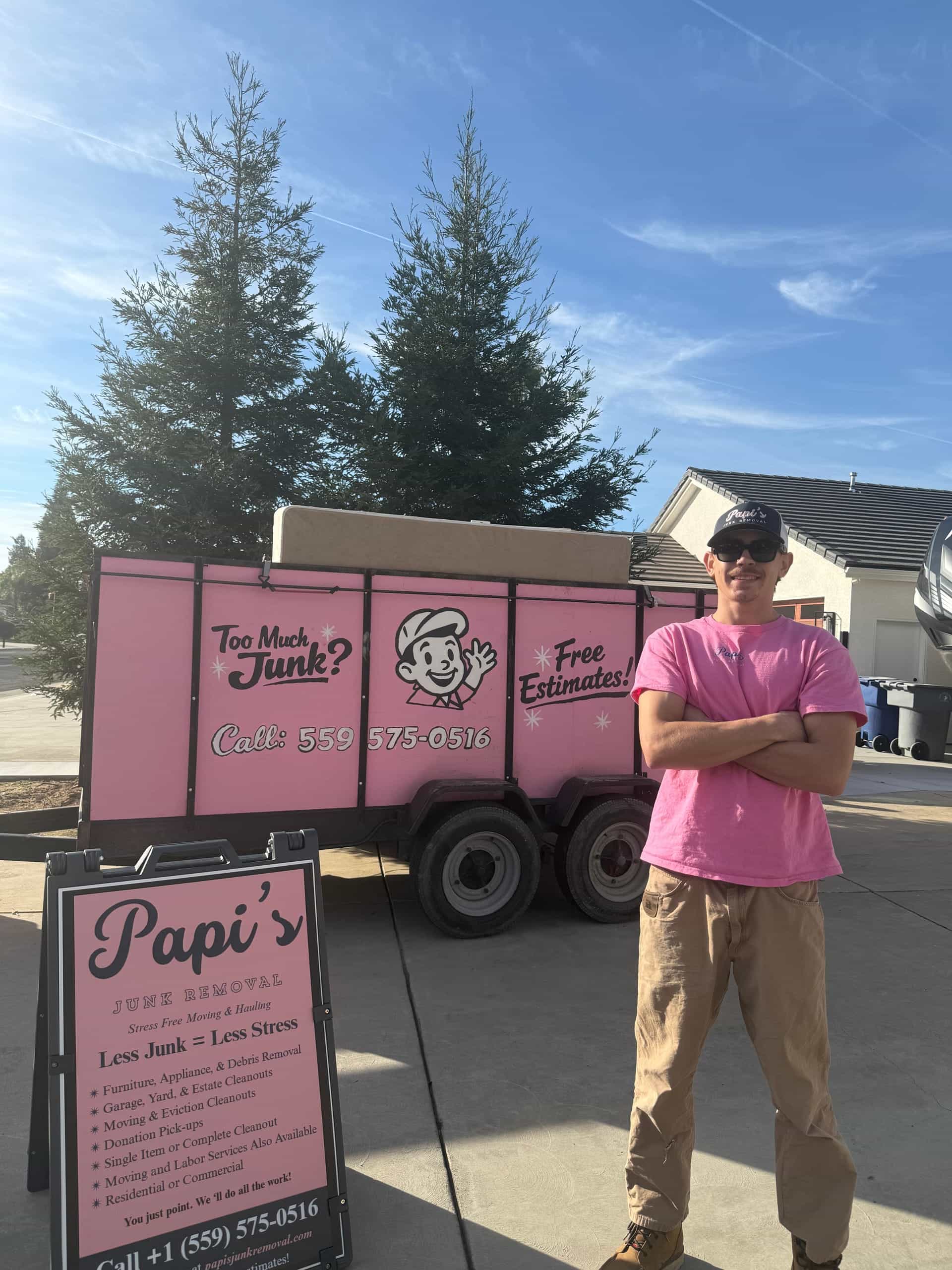 Papi's crew member in a pink shirt in front of the pink enclosed trailer and Papi's yard sign
