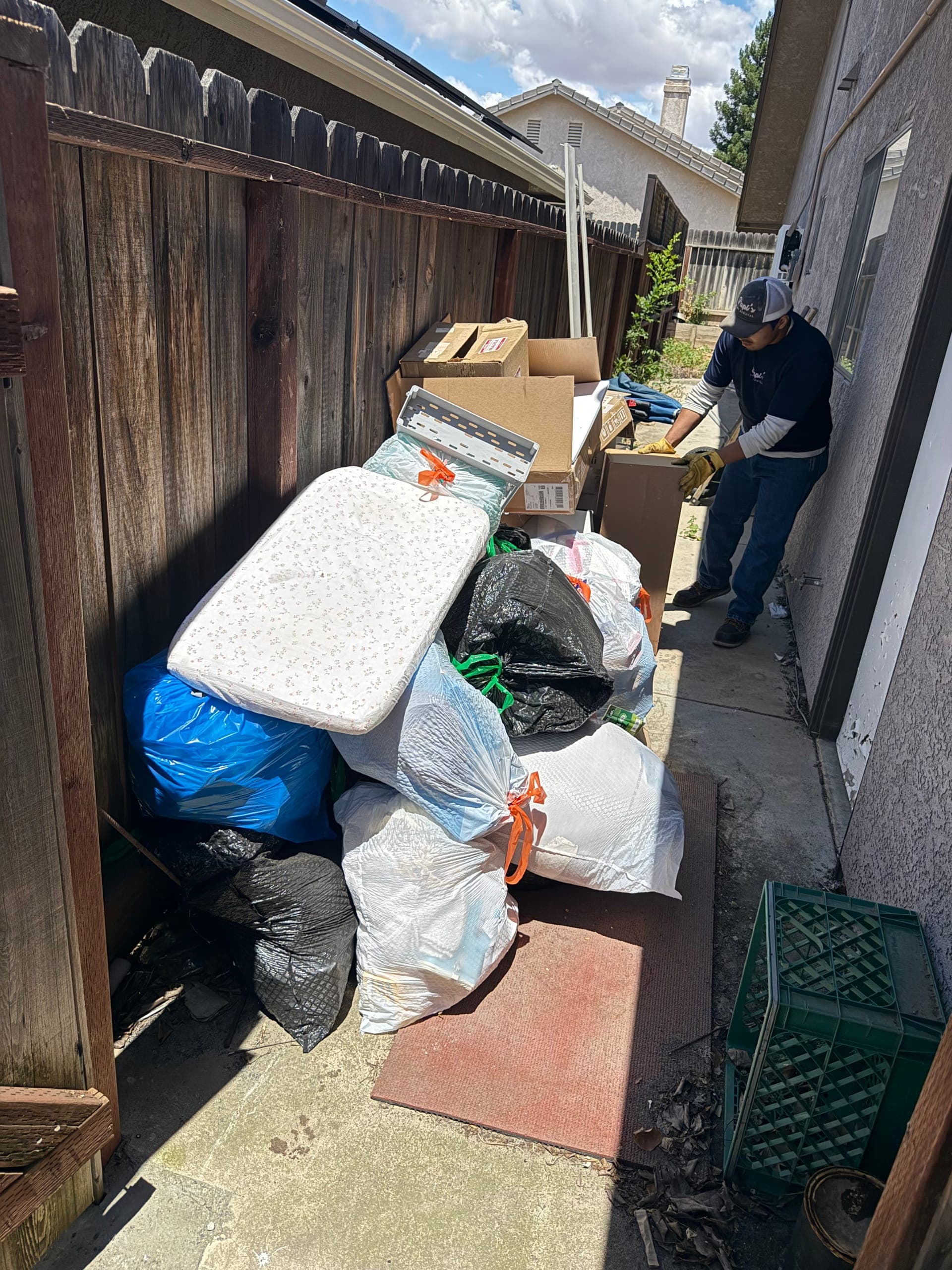 Papi's crew member clearing a narrow side yard full of mattresses, boxes and bagged junk