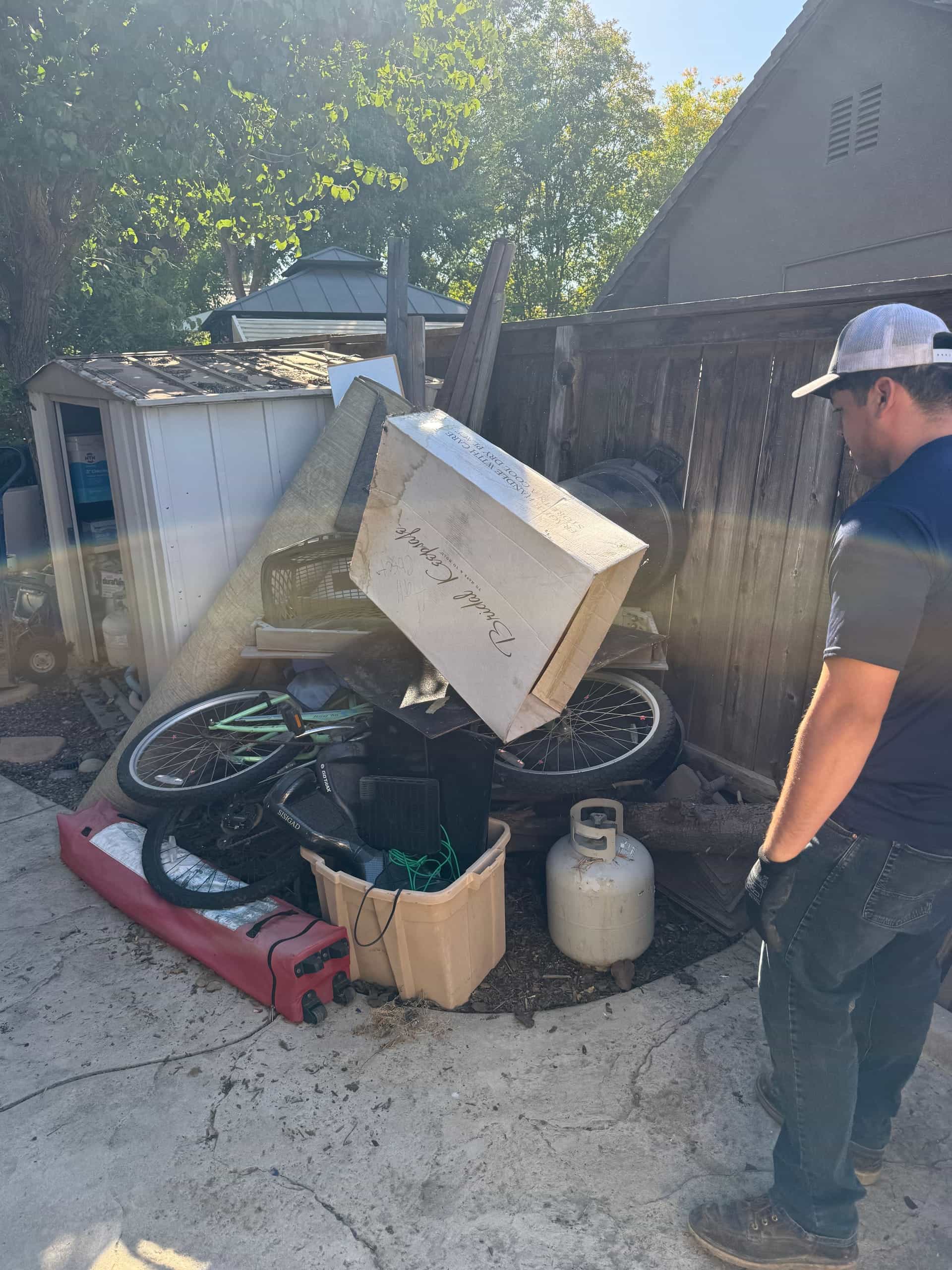 Papi's crew member sizing up a side-yard pile with a bike, propane tank and boxes near Clovis