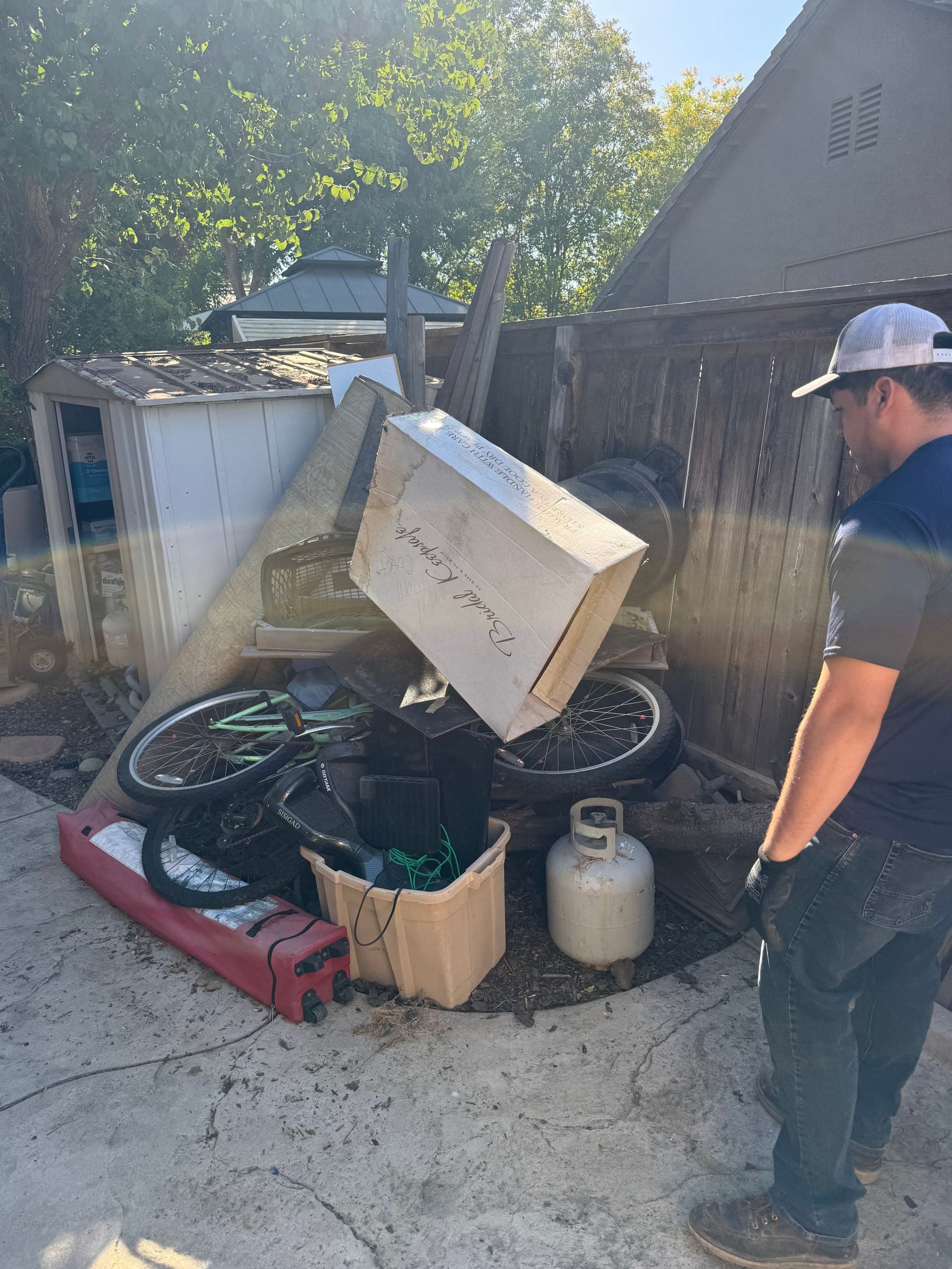 Papi's crew member sizing up a side-yard pile with a bike, propane tank and boxes near Clovis