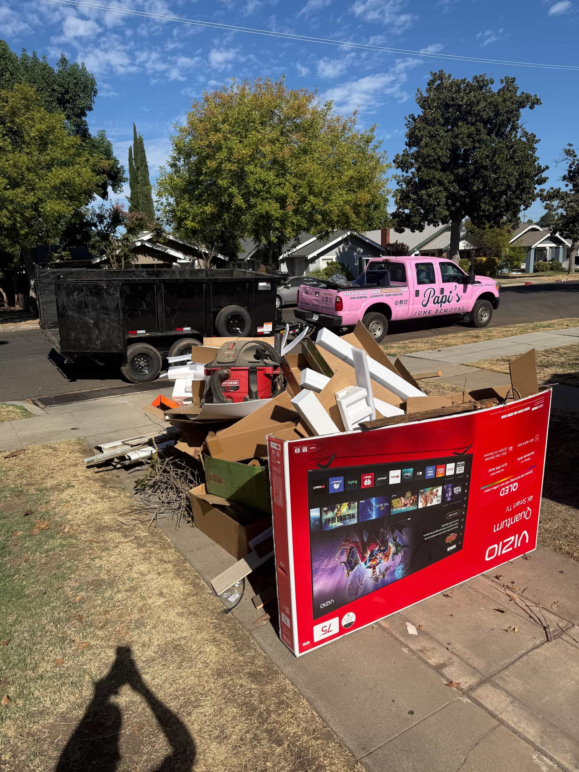 Curbside pile of a big TV box, cardboard and household junk in Fresno before Papi's pickup
