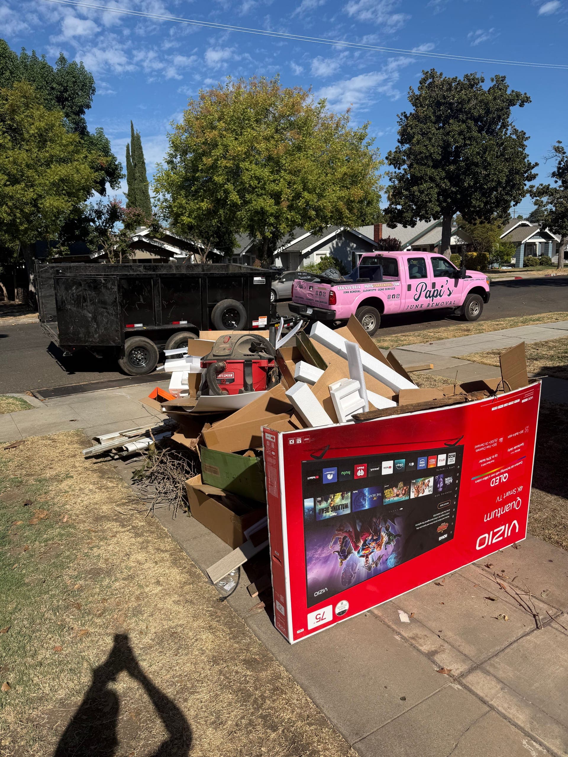 Curbside pile of a big TV box, cardboard and household junk in Fresno before Papi's pickup