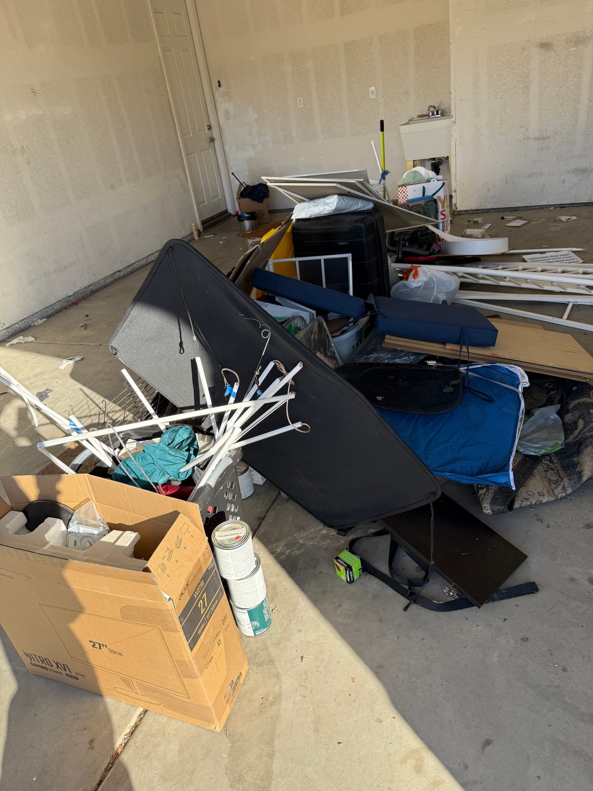 Garage floor covered in a broken trampoline, boxes, a suitcase and household junk