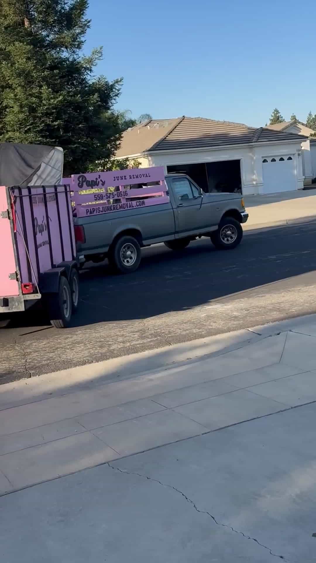 La camioneta de Papi's Junk Removal jalando el tráiler rosa por una calle de Clovis