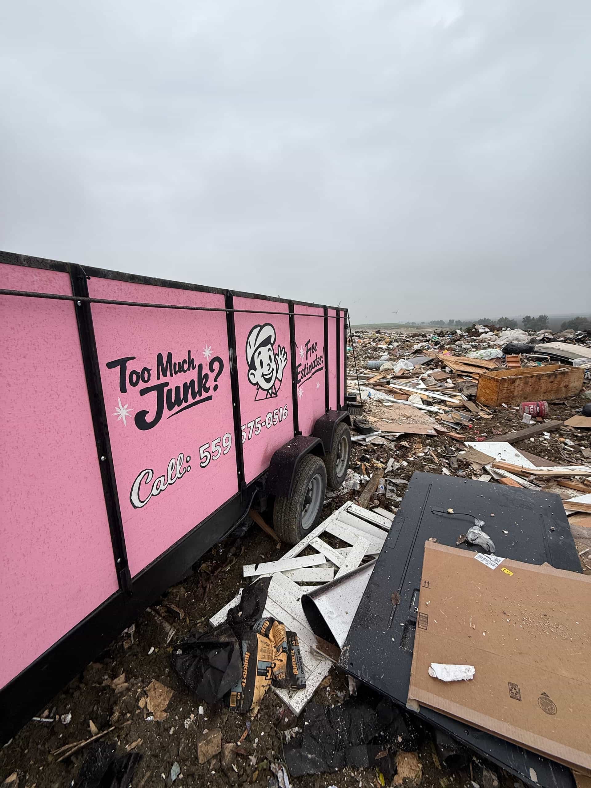 Side of the pink Papi's trailer at the dump, with debris in the background