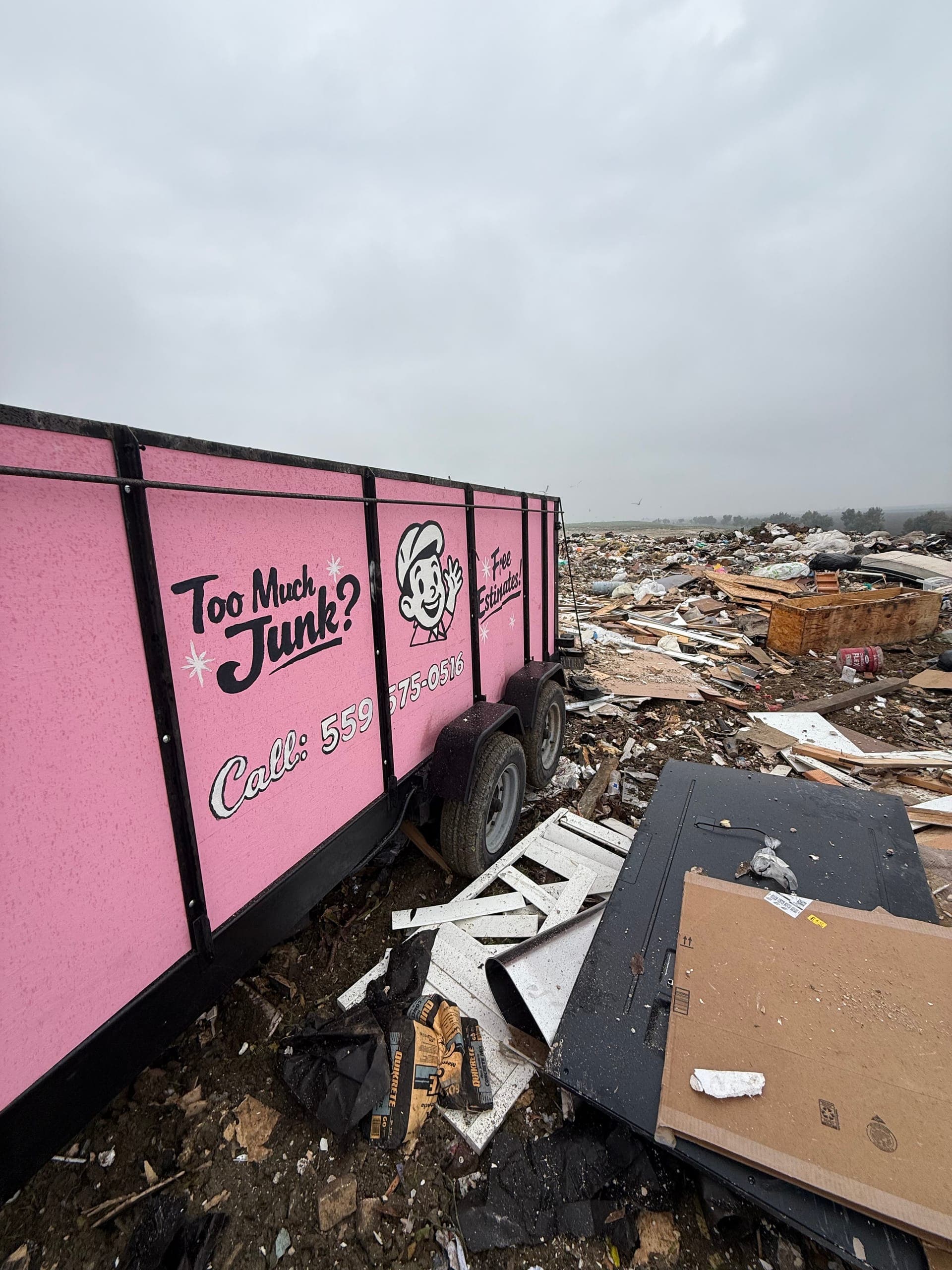 Side of the pink Papi's trailer at the dump, with debris in the background