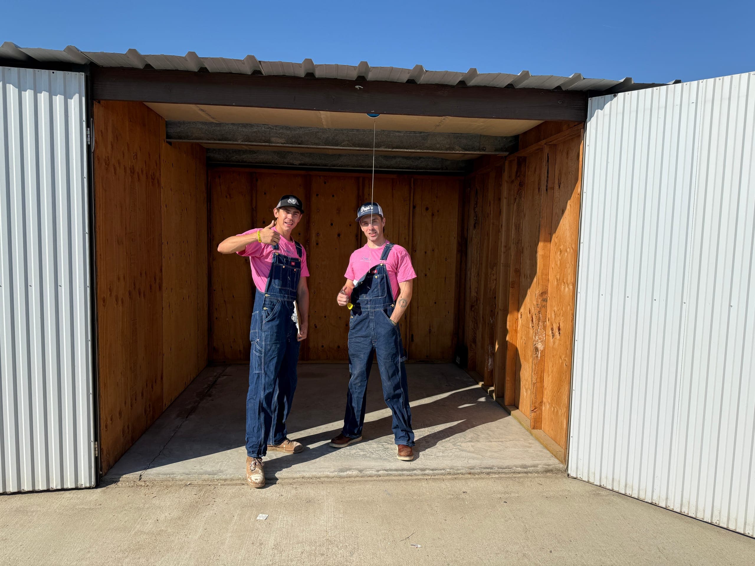 Two Papi's crew members in pink shirts and overalls inside an emptied storage unit