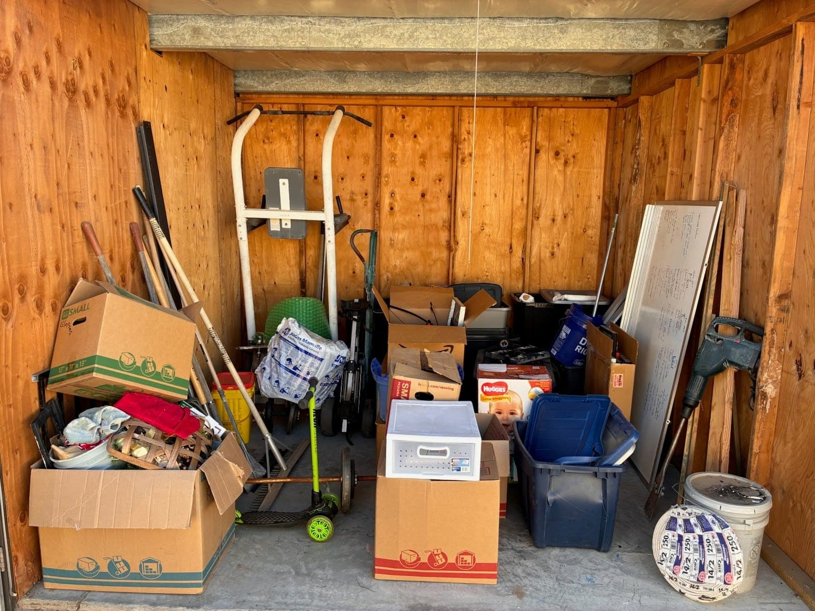 Storage unit packed with boxes, bins, a dolly and tools before a Papi's cleanout