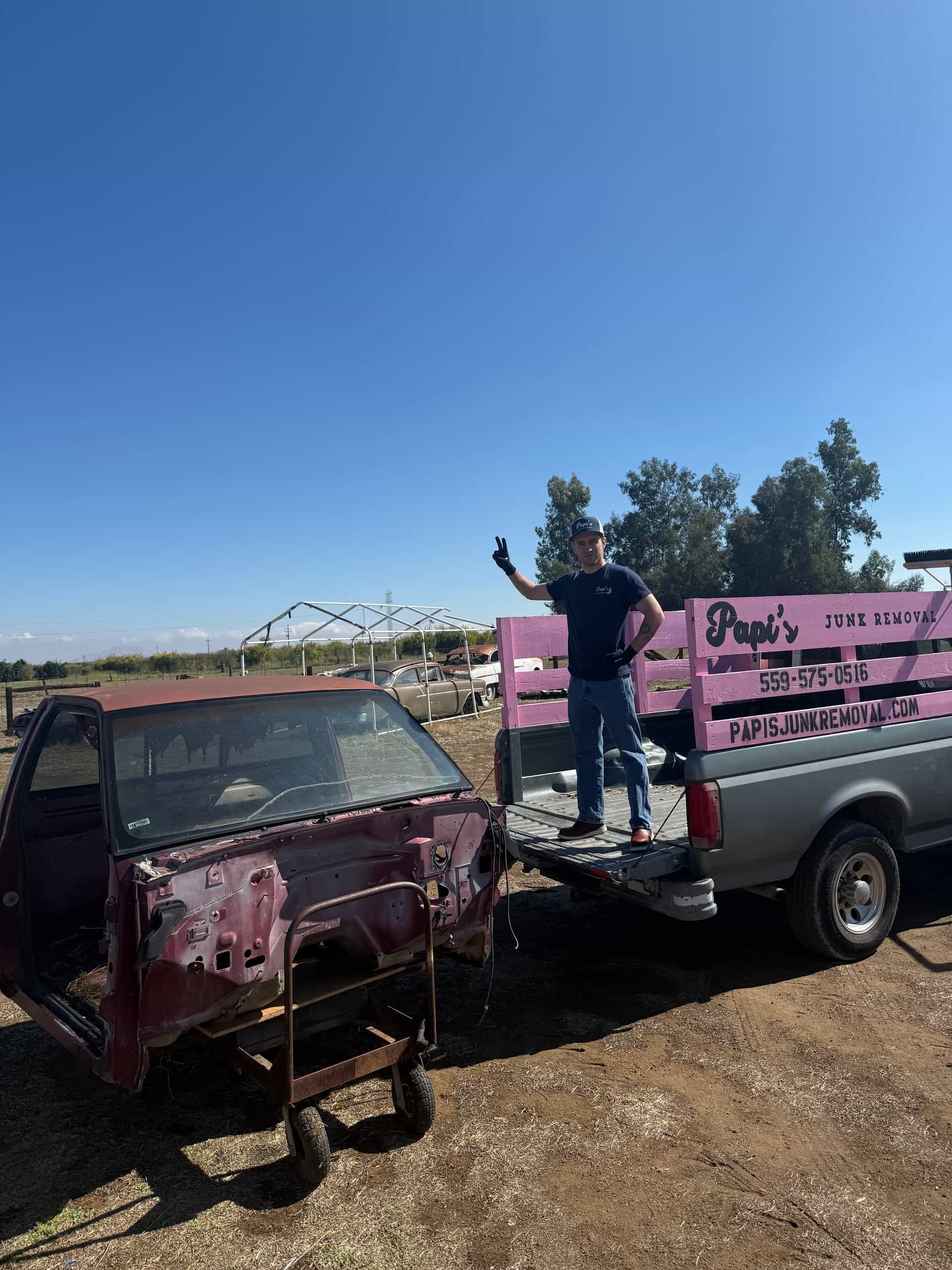 Papi's crew member on the truck bed next to an old pickup being hauled from a rural lot
